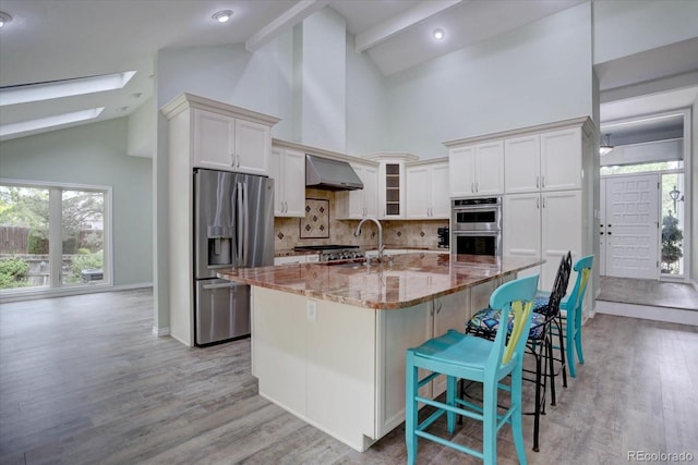 7715 S Hudson Ct, Centennial, CO 80122 - kitchen featuring appliances with stainless steel finishes, wall chimney range hood, high vaulted ceiling, backsplash, and light stone counters
