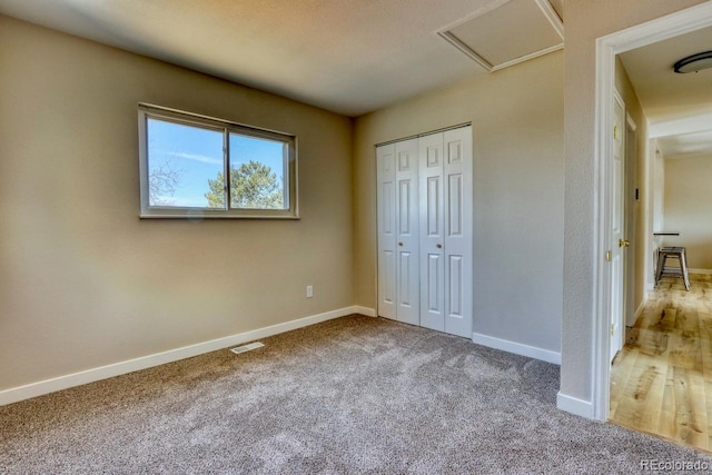 unfurnished bedroom featuring visible vents, baseboards, attic access, carpet floors, and a closet