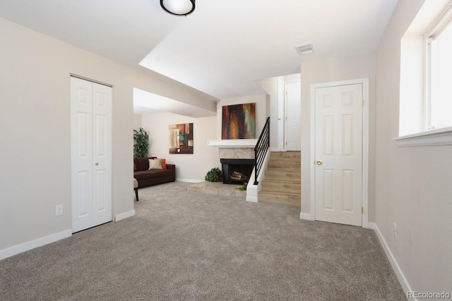 unfurnished room featuring baseboards, visible vents, stairs, a tiled fireplace, and carpet flooring