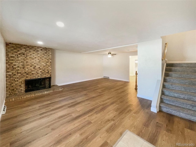 unfurnished living room featuring ceiling fan, hardwood / wood-style floors, and a brick fireplace