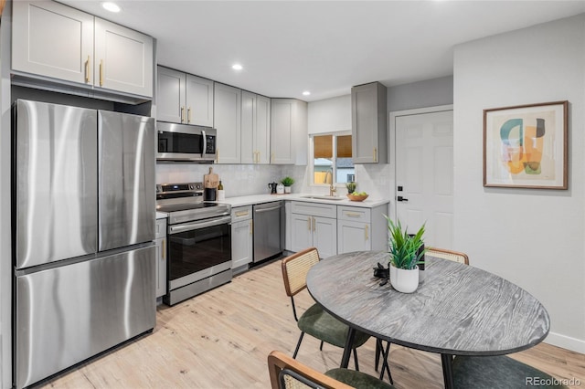 kitchen featuring appliances with stainless steel finishes, light wood-type flooring, gray cabinets, and tasteful backsplash