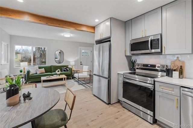 kitchen featuring backsplash, gray cabinets, appliances with stainless steel finishes, beamed ceiling, and light hardwood / wood-style floors