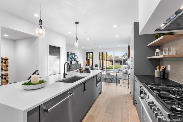 kitchen featuring light wood-type flooring, stainless steel appliances, extractor fan, sink, and decorative light fixtures