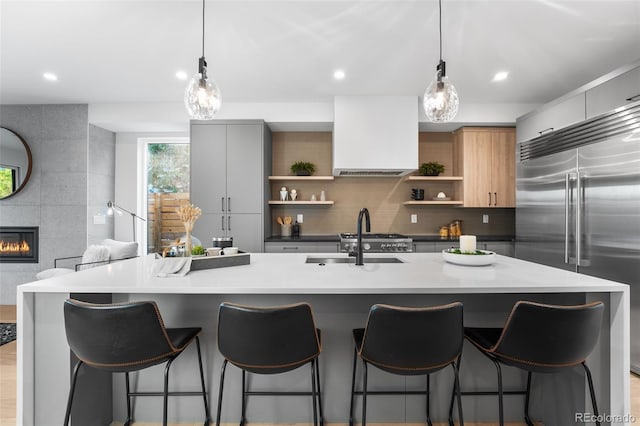 kitchen featuring a tiled fireplace, stainless steel built in fridge, hanging light fixtures, and ventilation hood