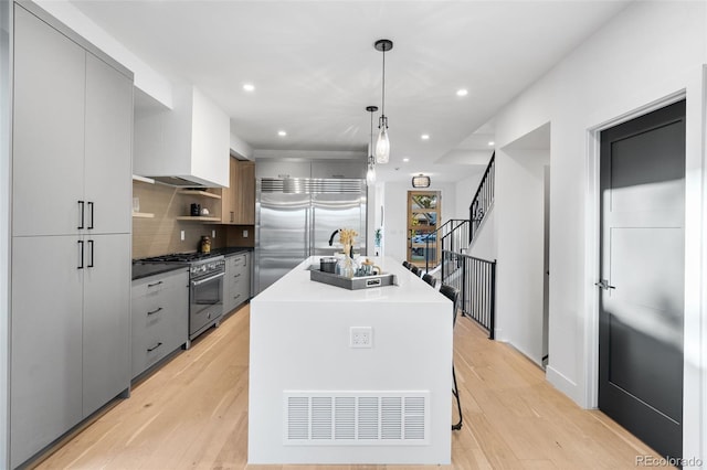 kitchen with gray cabinetry, high quality appliances, light hardwood / wood-style flooring, decorative light fixtures, and a kitchen island