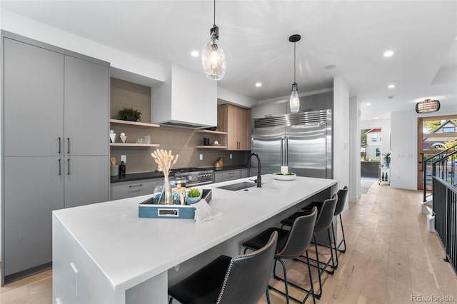 kitchen with a large island with sink, light hardwood / wood-style flooring, decorative light fixtures, custom range hood, and stainless steel appliances