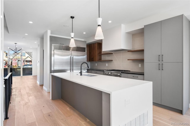 kitchen featuring custom range hood, sink, decorative light fixtures, light hardwood / wood-style floors, and an island with sink