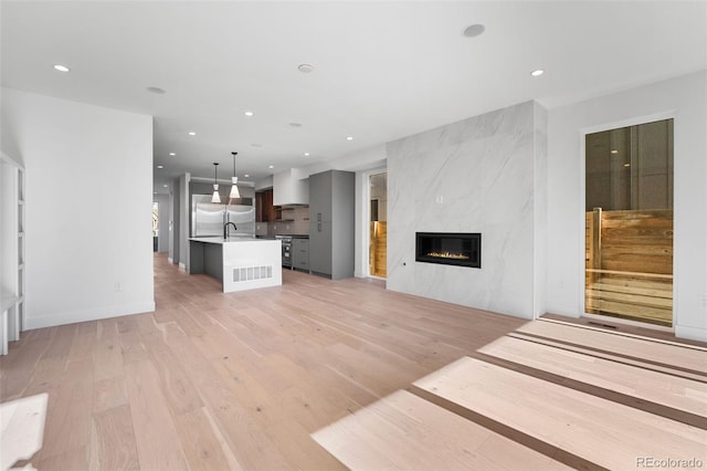 unfurnished living room with a high end fireplace, light wood-type flooring, and sink