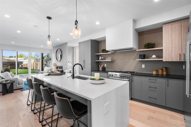 kitchen featuring a kitchen bar, gray cabinets, high end stainless steel range, and an island with sink