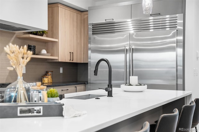 kitchen with light brown cabinetry, tasteful backsplash, sink, pendant lighting, and built in fridge