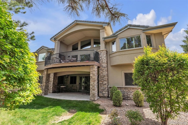 rear view of house with a balcony, stucco siding, a patio, and stone siding
