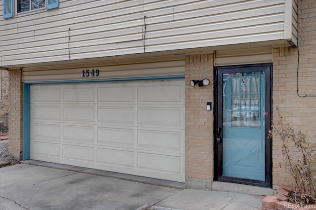 property entrance featuring a garage, concrete driveway, and brick siding