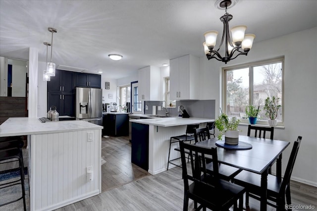 kitchen with light wood finished floors, light countertops, a sink, stainless steel fridge, and a peninsula