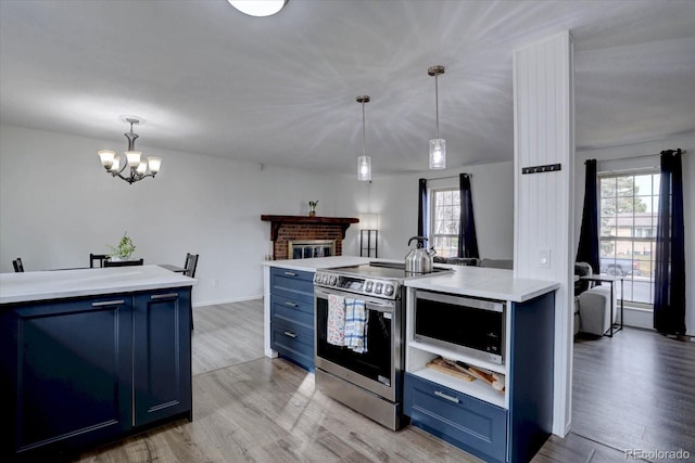 kitchen featuring blue cabinetry, light countertops, appliances with stainless steel finishes, light wood-style floors, and a brick fireplace