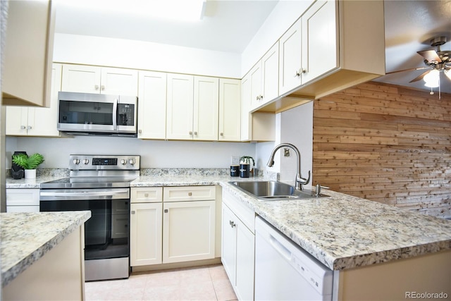 kitchen featuring ceiling fan, light tile patterned floors, light stone counters, stainless steel appliances, and a sink