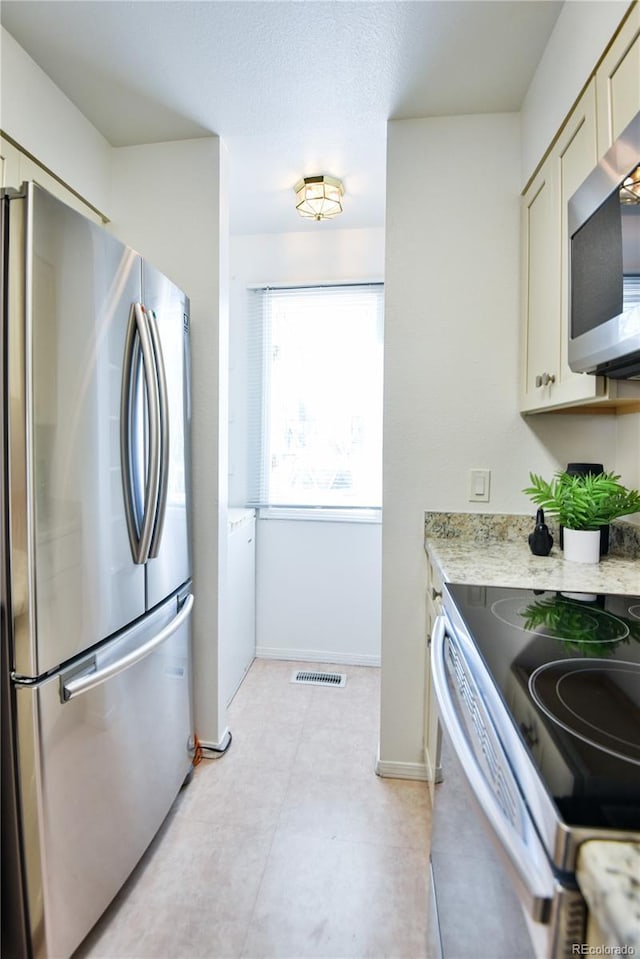 kitchen featuring baseboards, visible vents, light stone counters, cream cabinets, and stainless steel appliances