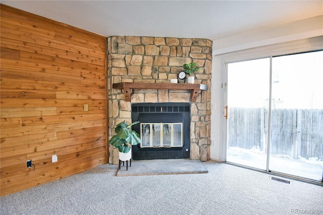 unfurnished living room with visible vents, carpet flooring, a fireplace, and wood walls