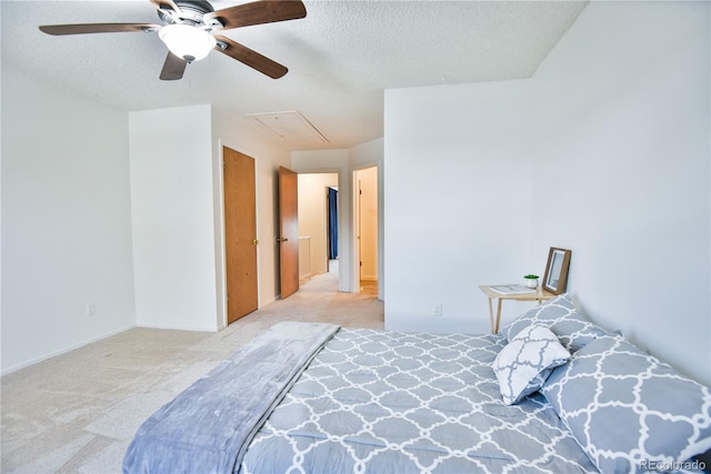 bedroom featuring attic access, light colored carpet, a textured ceiling, and a ceiling fan