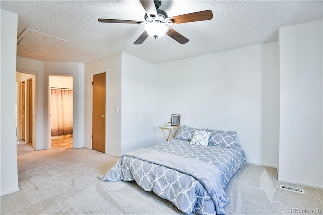 bedroom featuring light carpet, a textured ceiling, visible vents, and attic access