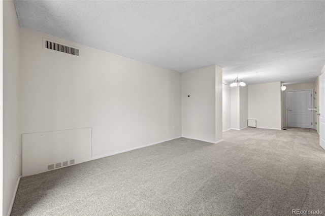 carpeted spare room featuring a textured ceiling and a notable chandelier