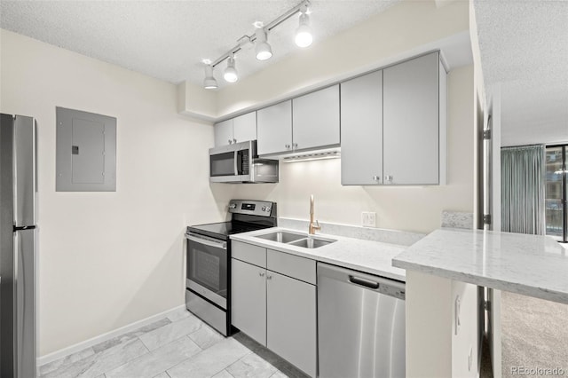 kitchen with appliances with stainless steel finishes, sink, electric panel, light stone countertops, and a textured ceiling