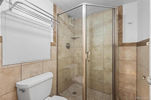 bathroom featuring toilet, an enclosed shower, and tile walls