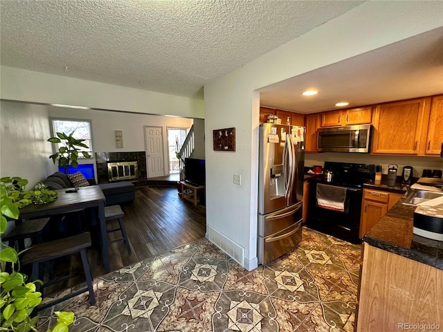 11576 E Bayaud Dr, Aurora, CO 80012 - kitchen with appliances with stainless steel finishes, dark countertops, open floor plan, brown cabinetry, and a textured ceiling