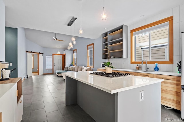 kitchen with sink, a center island, hanging light fixtures, a barn door, and stainless steel gas stovetop