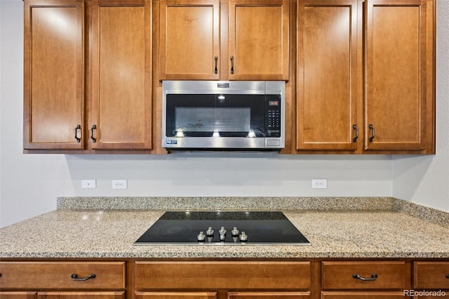 17710 E Emilia Dr, Parker, CO 80134 - kitchen featuring stainless steel microwave, black electric cooktop, light stone counters, and brown cabinetry