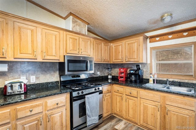 kitchen featuring lofted ceiling, stainless steel appliances, sink, and dark stone countertops