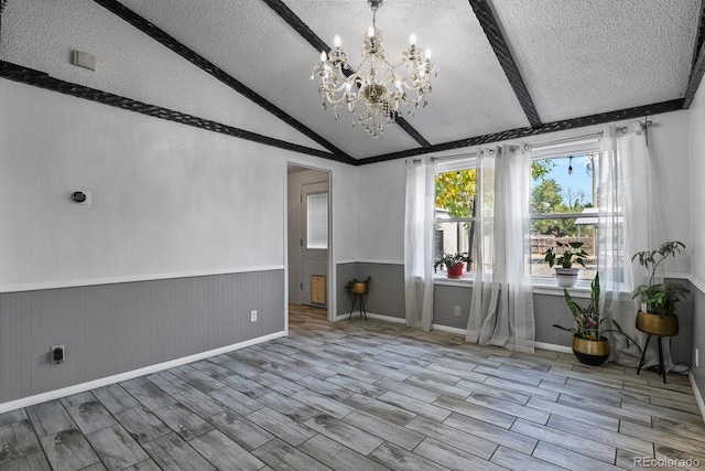 unfurnished room featuring a chandelier, vaulted ceiling with beams, light wood-type flooring, and a textured ceiling