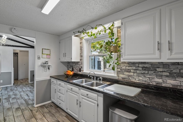 kitchen featuring lofted ceiling, light hardwood / wood-style floors, white cabinets, and sink