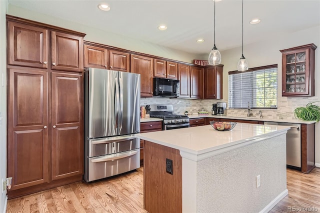 kitchen featuring appliances with stainless steel finishes, sink, a kitchen island, decorative light fixtures, and light hardwood / wood-style floors