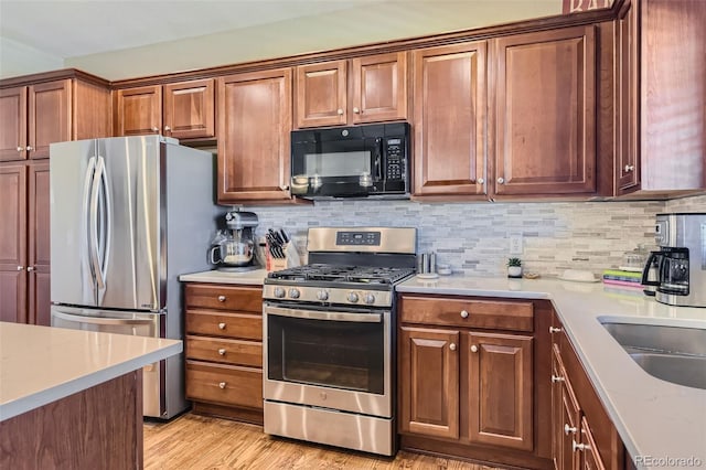 kitchen with light wood-type flooring, sink, stainless steel appliances, and decorative backsplash