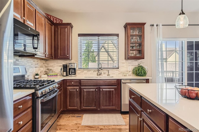 kitchen featuring sink, light wood-type flooring, pendant lighting, stainless steel appliances, and tasteful backsplash