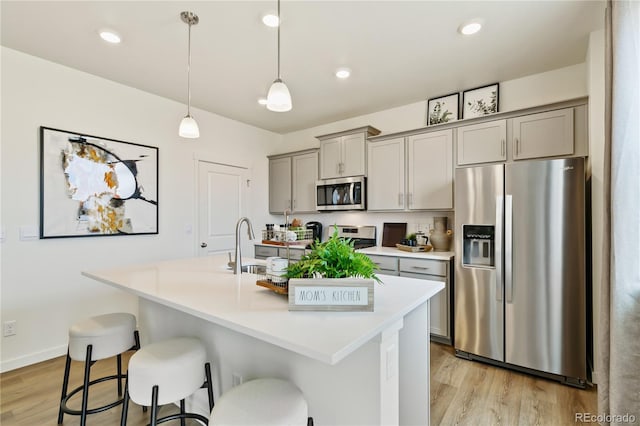 kitchen with pendant lighting, stainless steel appliances, gray cabinets, and a center island with sink