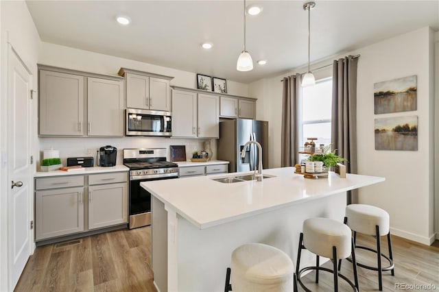 kitchen featuring a kitchen bar, sink, gray cabinetry, stainless steel appliances, and a kitchen island with sink