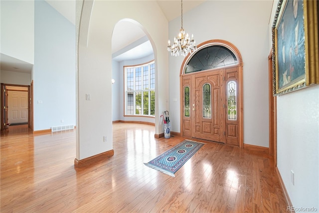 foyer entrance with high vaulted ceiling, a chandelier, and light wood-type flooring