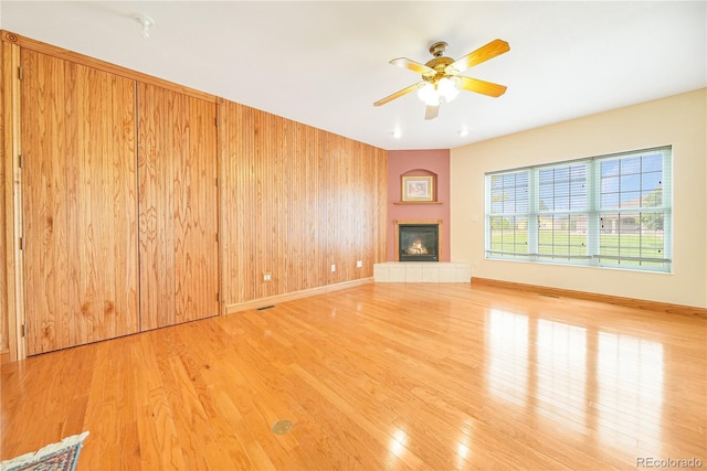 unfurnished living room with light hardwood / wood-style floors, a tile fireplace, ceiling fan, and wood walls