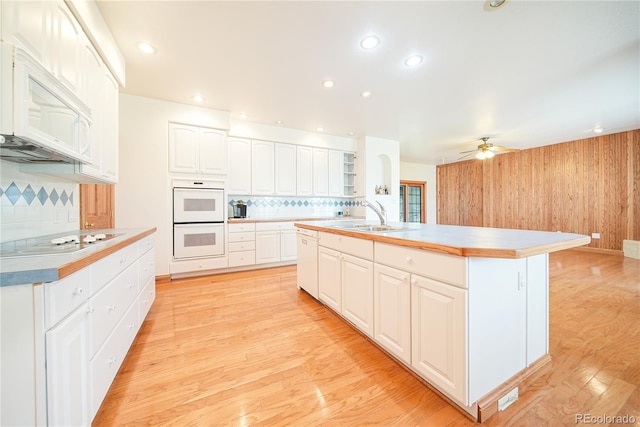 kitchen featuring sink, white cabinetry, an island with sink, white appliances, and light hardwood / wood-style floors