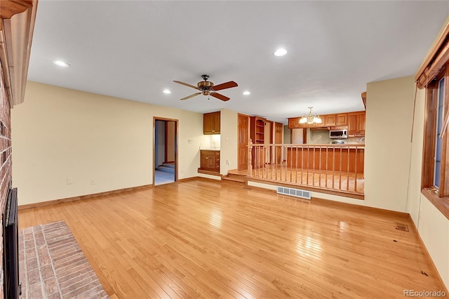 unfurnished living room featuring ceiling fan with notable chandelier, light hardwood / wood-style floors, and a brick fireplace