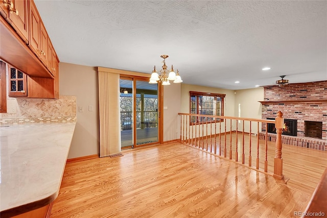 dining area with ceiling fan with notable chandelier, light wood-type flooring, a textured ceiling, and a brick fireplace