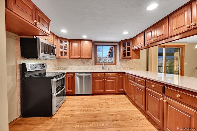 kitchen featuring sink, stainless steel appliances, light hardwood / wood-style flooring, kitchen peninsula, and decorative backsplash