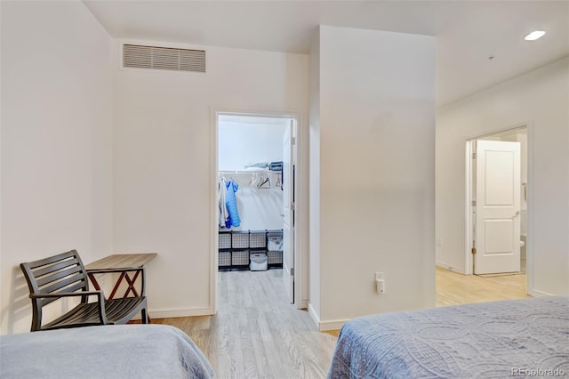 bedroom with light wood-type flooring, visible vents, baseboards, and a walk in closet