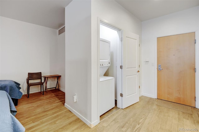 washroom featuring stacked washer / dryer, light wood finished floors, laundry area, and baseboards