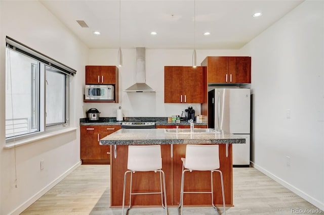 kitchen featuring light wood-style flooring, a sink, wall chimney exhaust hood, a center island with sink, and appliances with stainless steel finishes