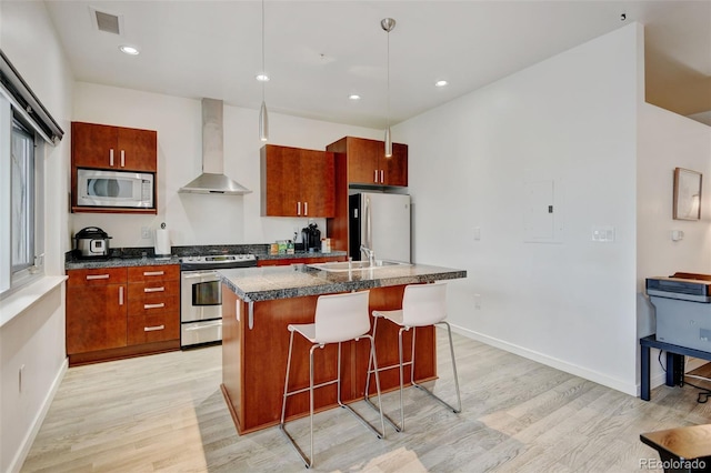 kitchen with a breakfast bar, wall chimney exhaust hood, light wood-type flooring, visible vents, and appliances with stainless steel finishes