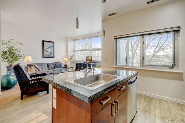 kitchen with a sink, dark countertops, stainless steel dishwasher, visible vents, and light wood-style floors