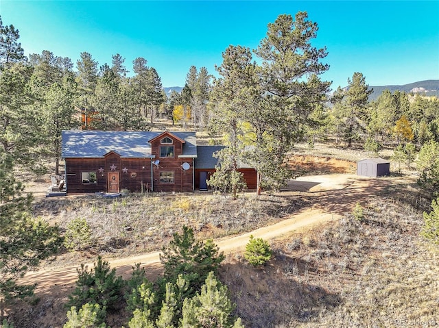 view of front of property with a storage shed, a forest view, and an outdoor structure