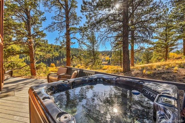 view of pool with a wooded view, hot tub deck surround, and a wooden deck